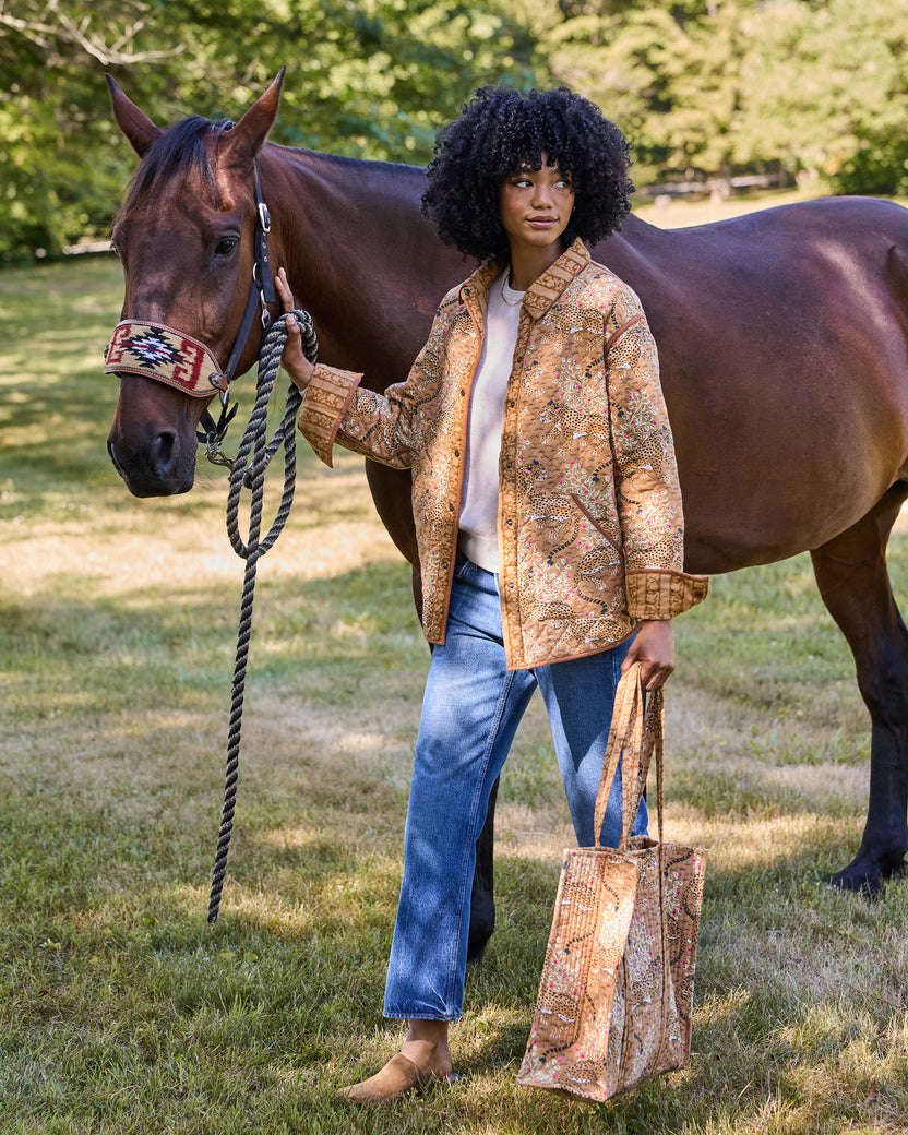 Person wearing a patterned quilted jacket and holding a horse’s lead rope outdoors.
