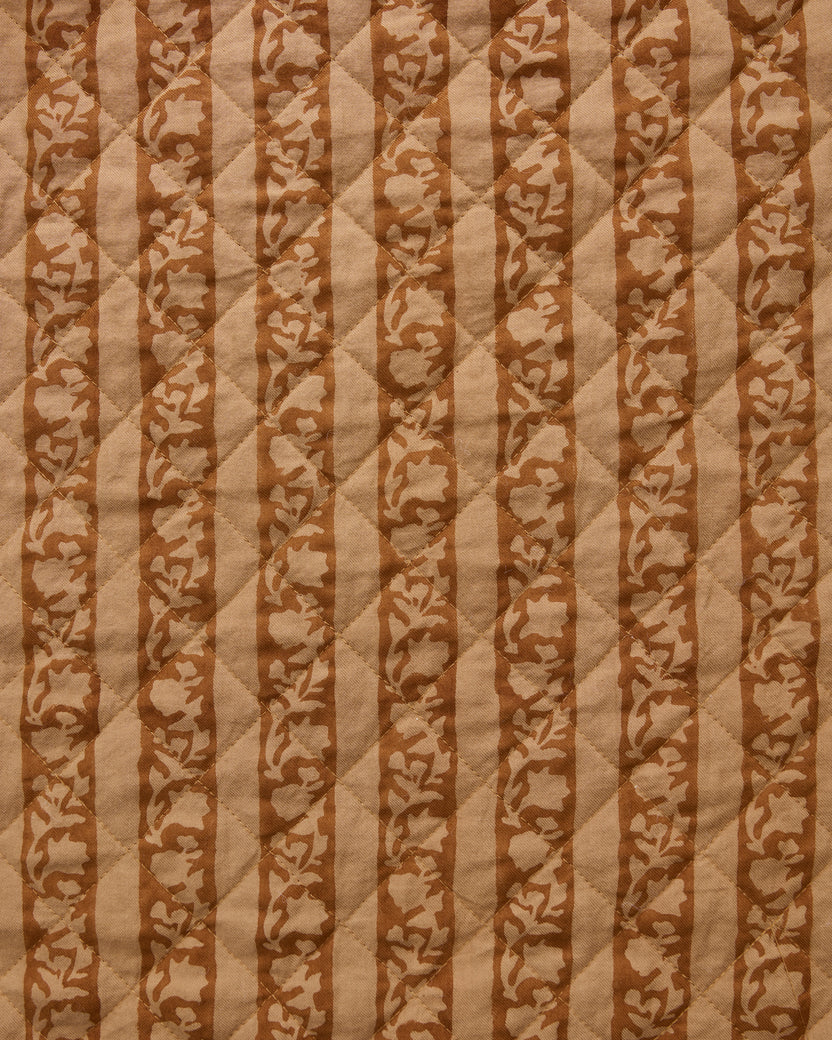Mustard Seed fabric swatch with alternating tan stripes and floral vine patterns on a quilted surface.