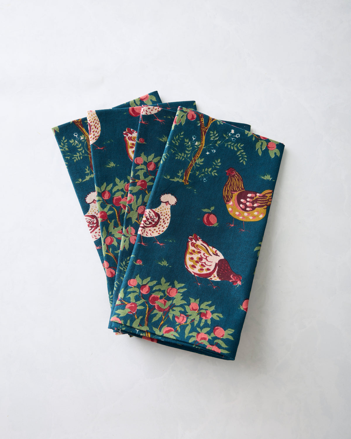 Four folded navy Hen House dinner napkins arranged in a fan, printed with chickens, apples, and trees.