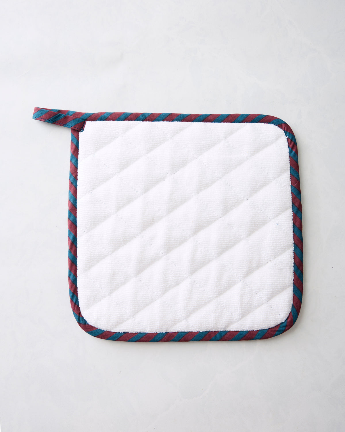 Back of the navy Hen House pot holder, showing a white quilted surface and striped edging.