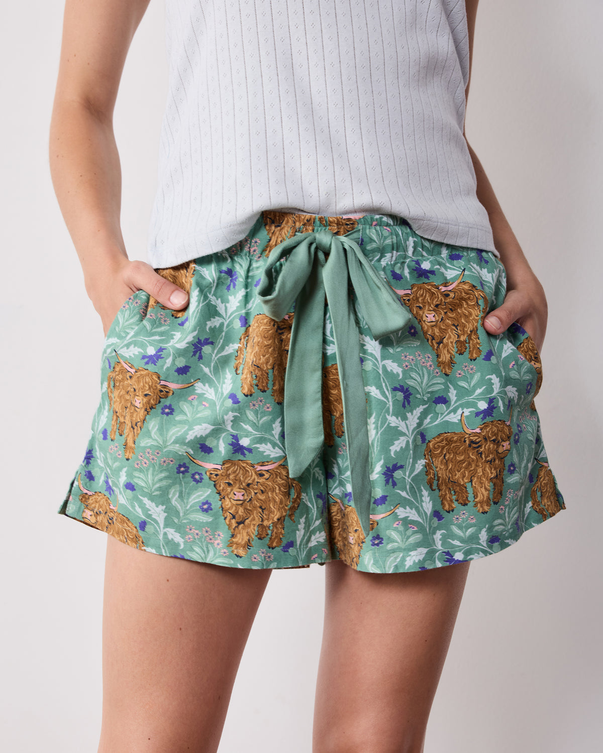 Close-up of green Highland cow-print pajama shorts showing the satin tie, elastic waistband, and pockets