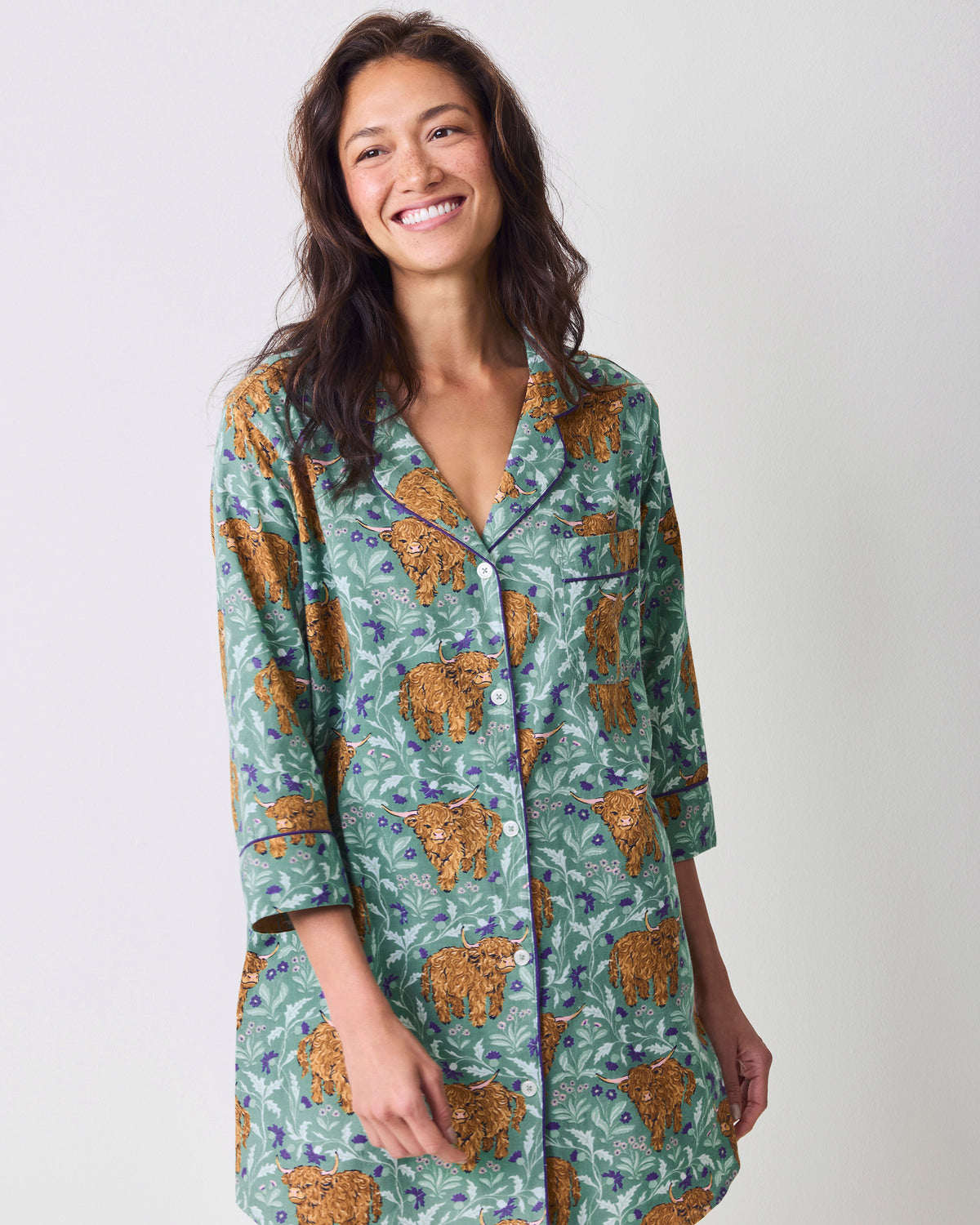 Front view of a model wearing a green Highland cow-print button-down sleep shirt.