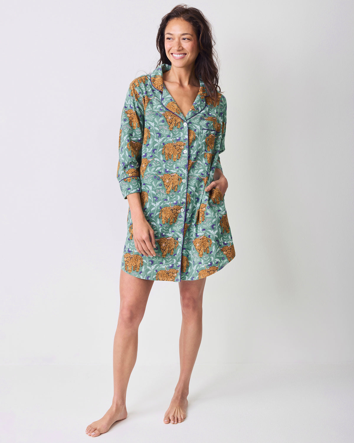 Full-length model wearing a green Highland cow-print button-down sleep shirt.