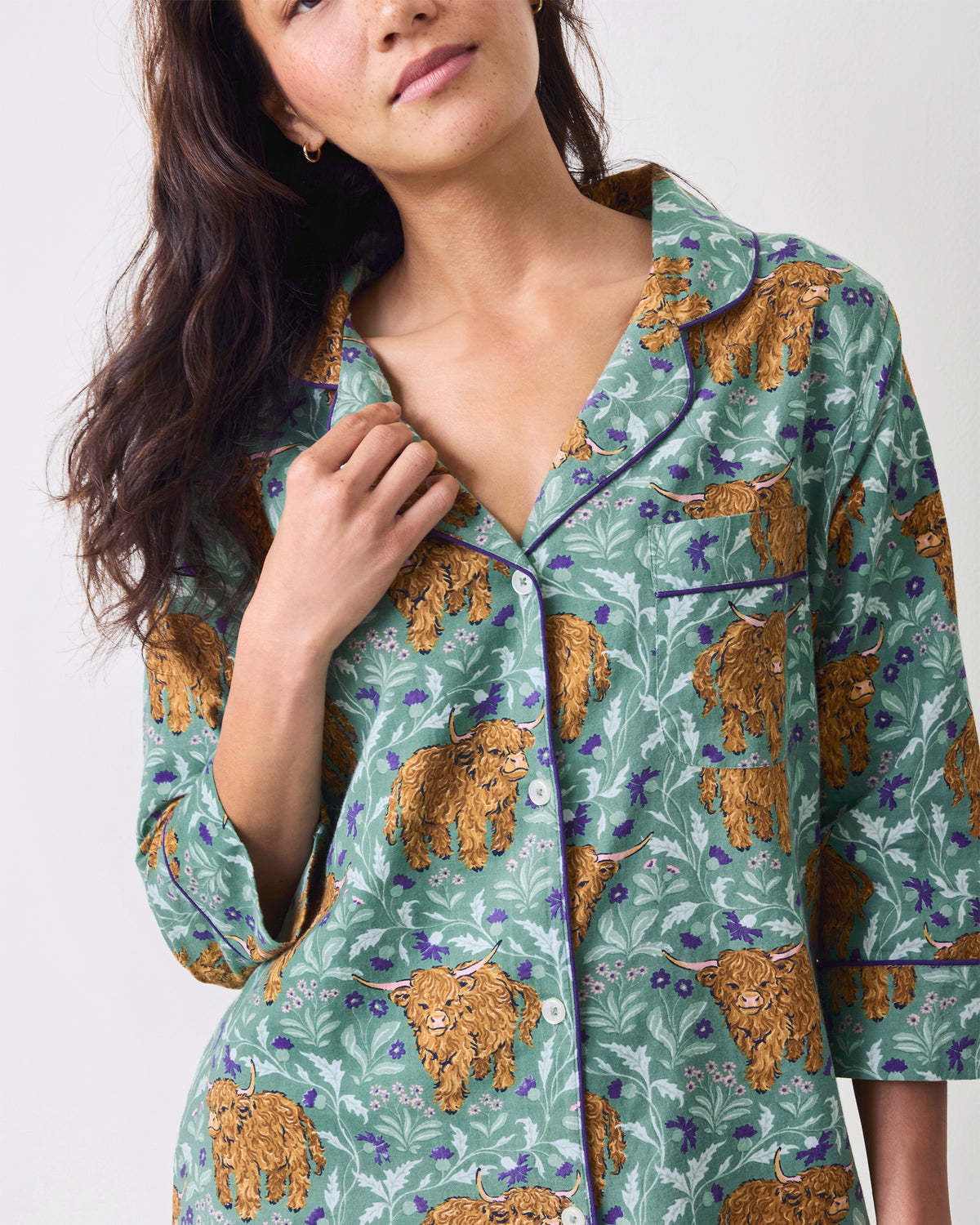 Close-up of the collar, buttons, chest pocket, and Highland cow print on a green sleep shirt.