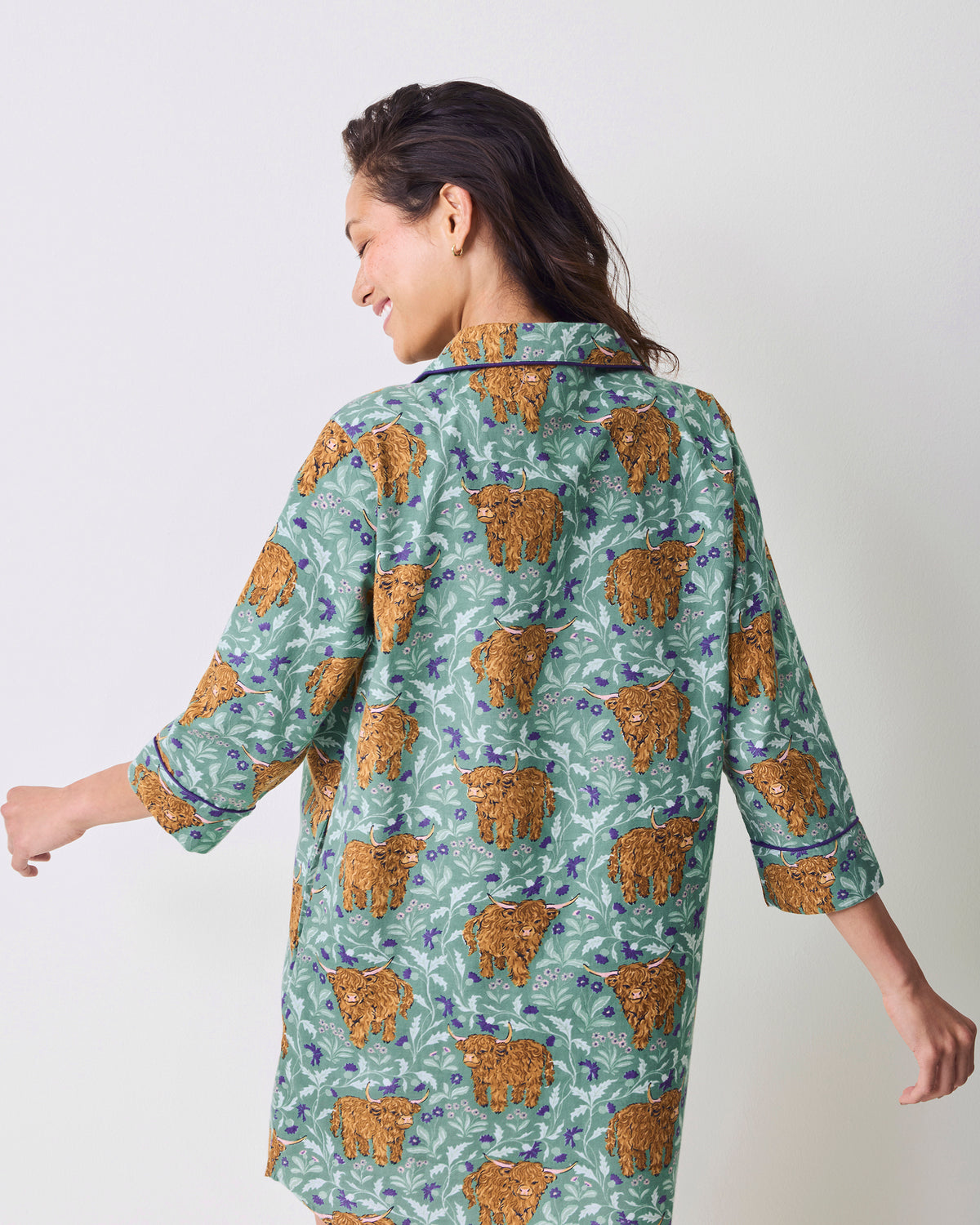 Back view of a model wearing a green Highland cow-print button-down sleep shirt.
