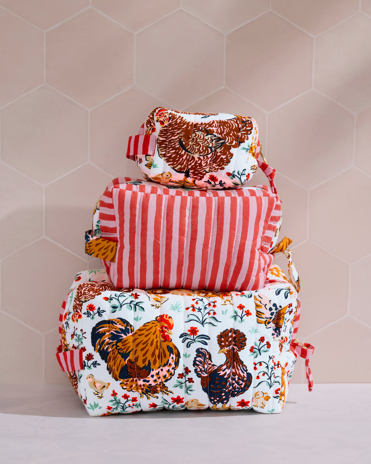 Three quilted pouches stacked together, with chicken and floral prints on the top and bottom pouches and red-and-white stripes on the middle pouch.
