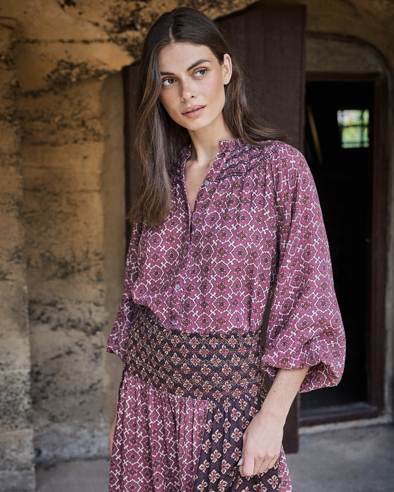 Person wearing the patterned Aspen blouse with voluminous sleeves and a high-waisted patterned skirt.
