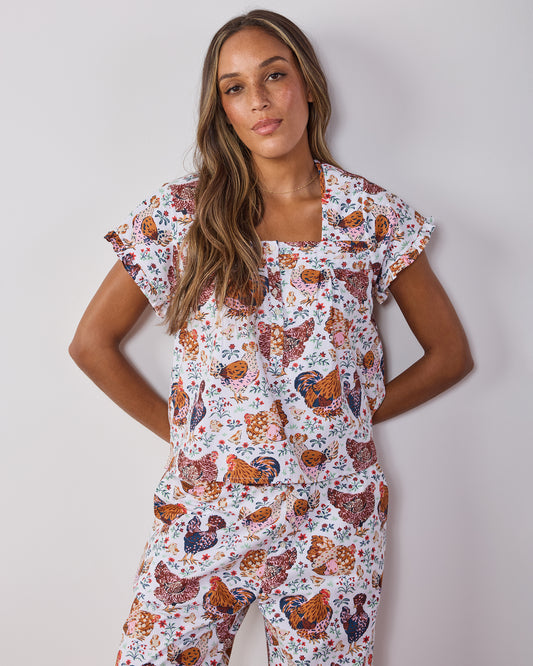 Model wearing a cropped pajama top with flutter sleeves and matching pants in a chicken-and-floral print.
