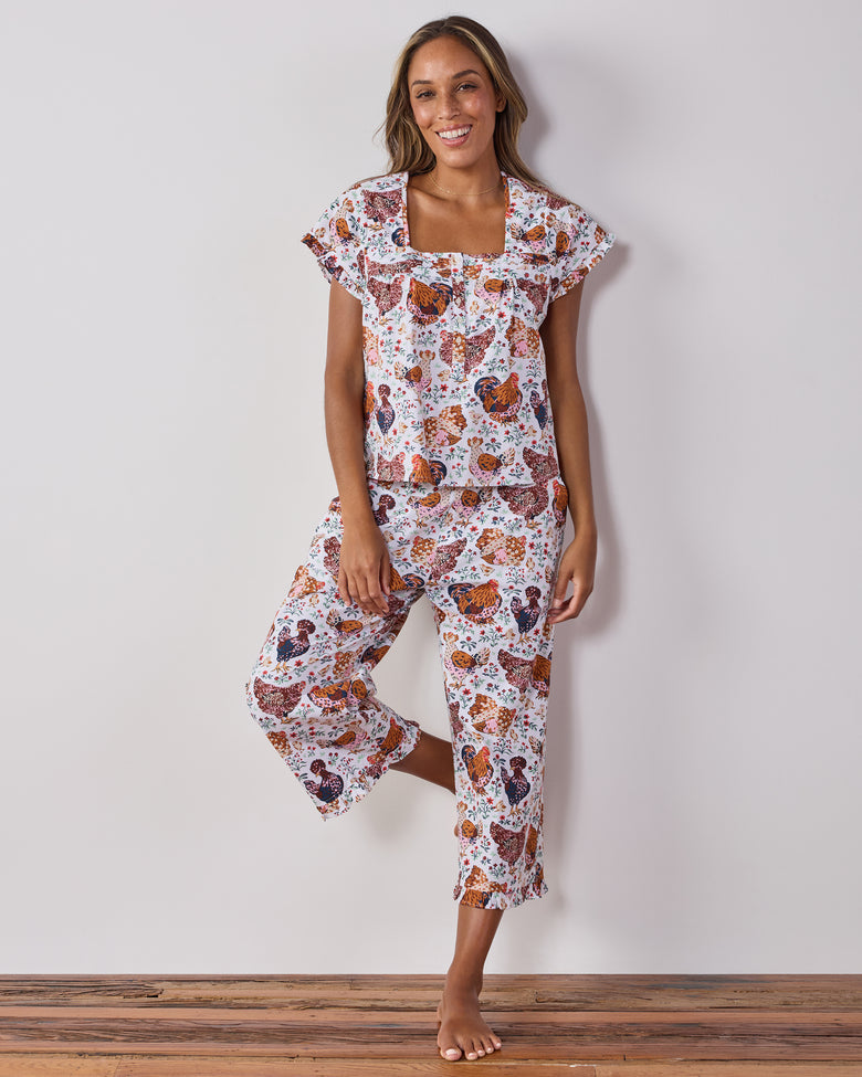 Front view of a person wearing a cropped short-sleeve top and cropped pants with a colorful chicken-and-floral print.