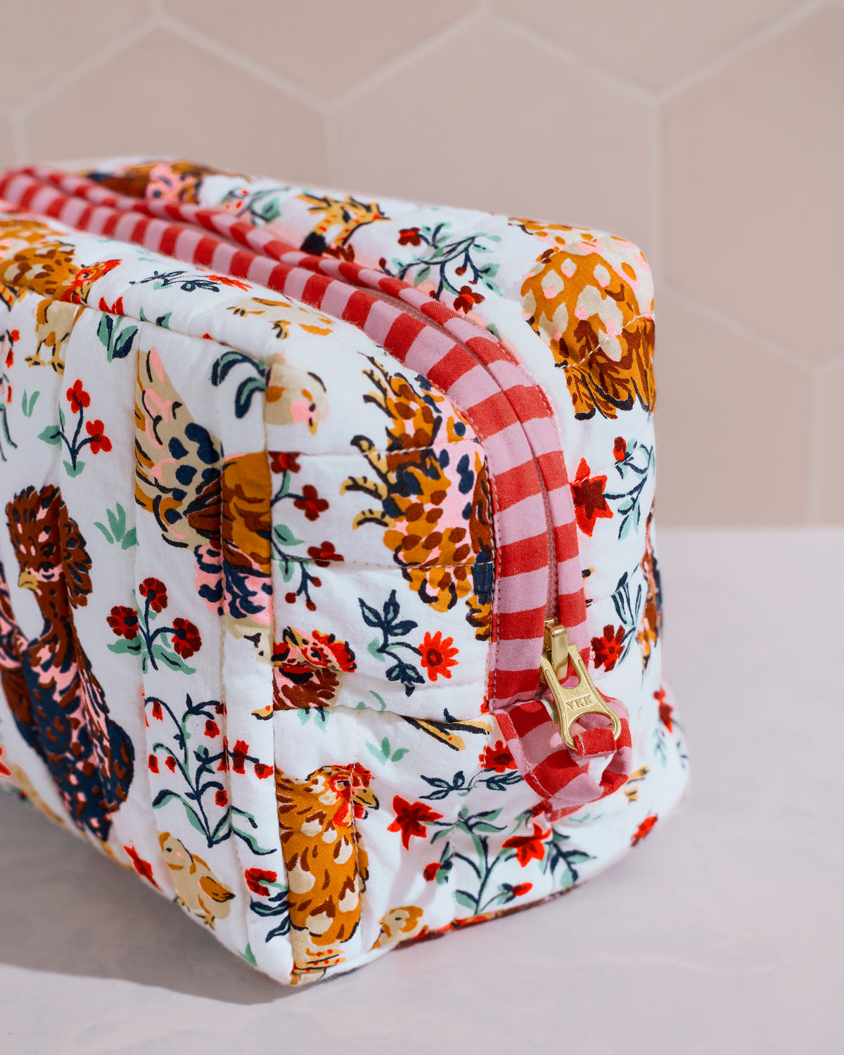 Close-up of the cloud quilted pouch showing its floral and chicken print, red-and-white striped zipper trim, and gold-toned zipper pull.