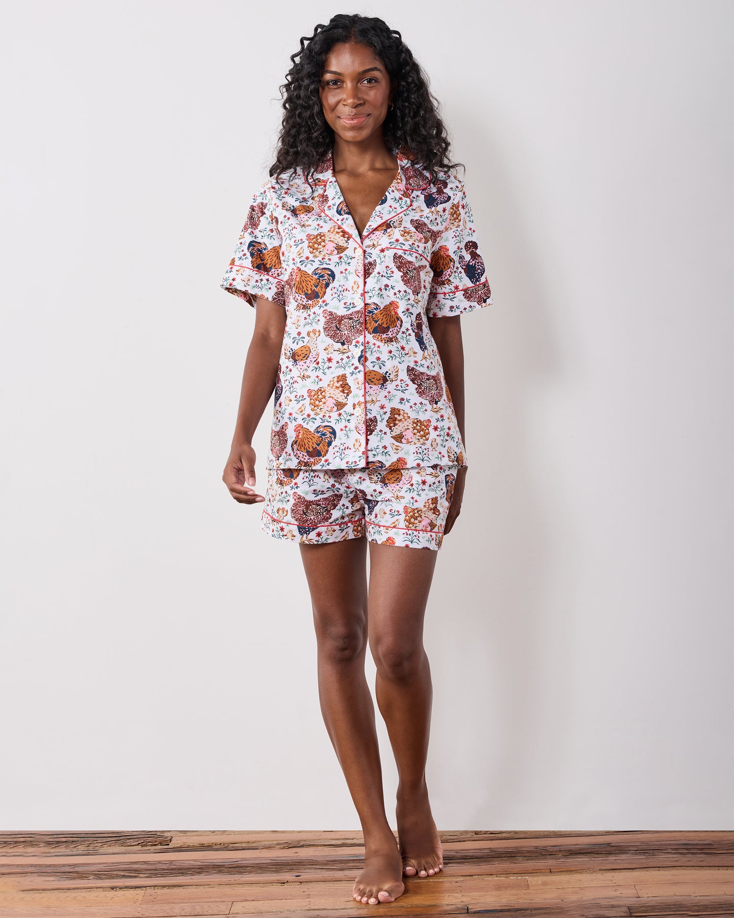 Model standing and wearing a short-sleeve pajama top with matching shorts in a chicken-and-floral print.