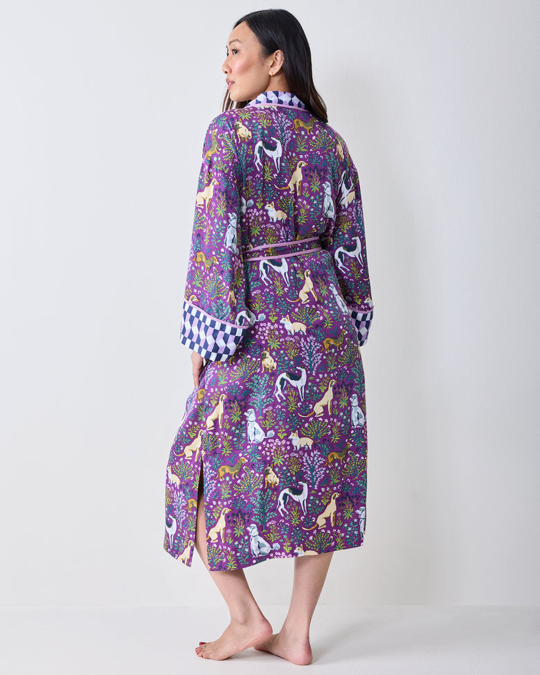 Back three-quarter view of a purple dog-and-floral print wrap robe showing the tied belt, contrasting sleeve cuffs, and side hem slit.