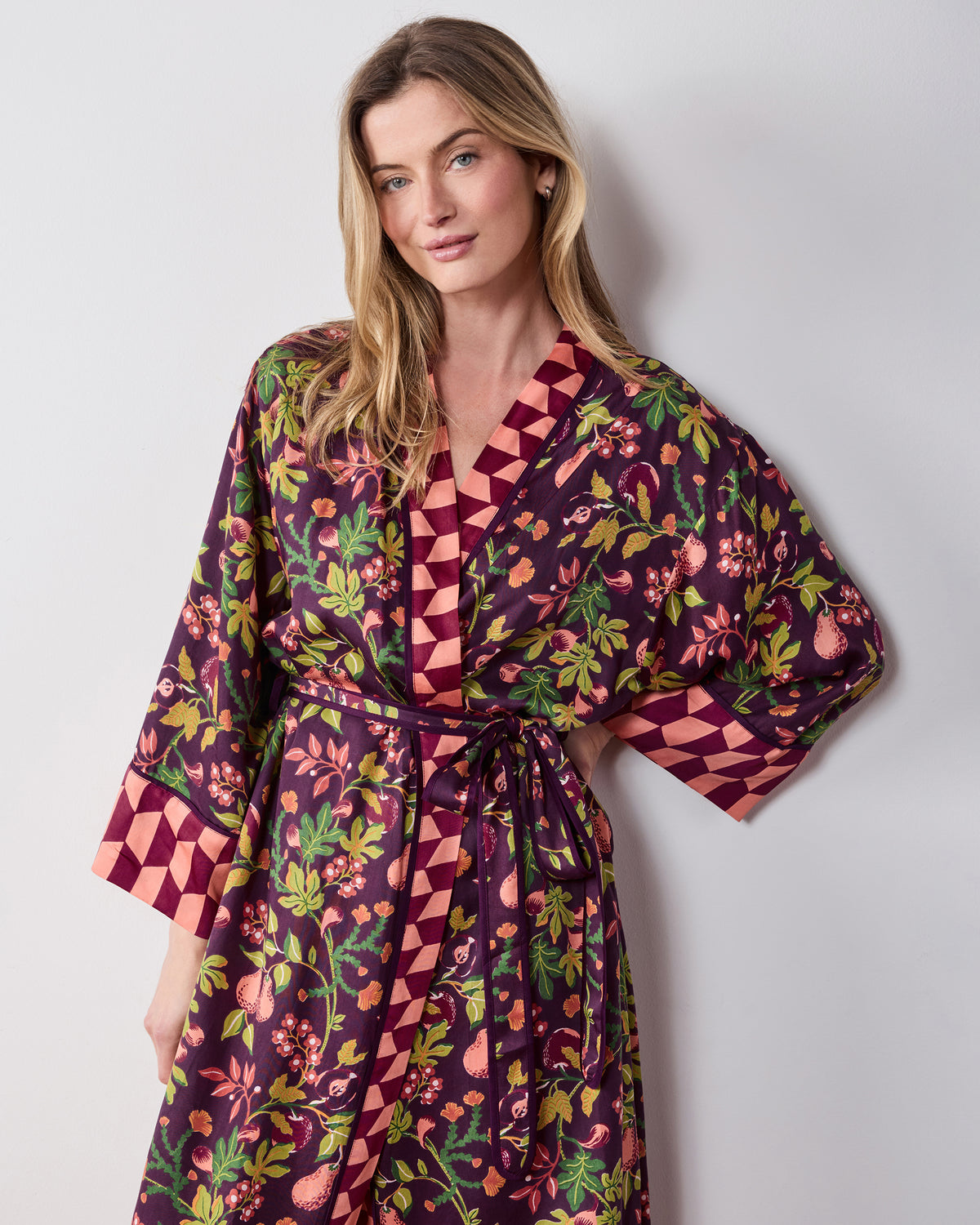 Front view of the plum Pomme & Poire robe with a contrasting geometric-trimmed neckline and cuffs, tied belt, and fruit-and-greenery print.