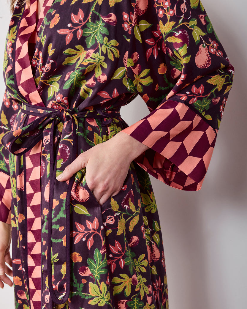 Close view of the plum Pomme & Poire robe showing its fruit-and-greenery print, tied belt, pocket, and contrasting geometric cuff.