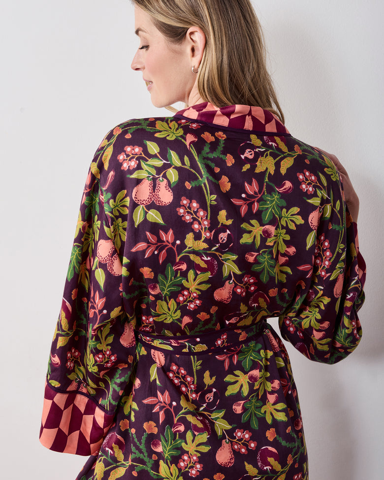 Back view of the plum Pomme & Poire robe showing the fruit-and-greenery print, tied belt, collar, and contrasting sleeve cuffs.