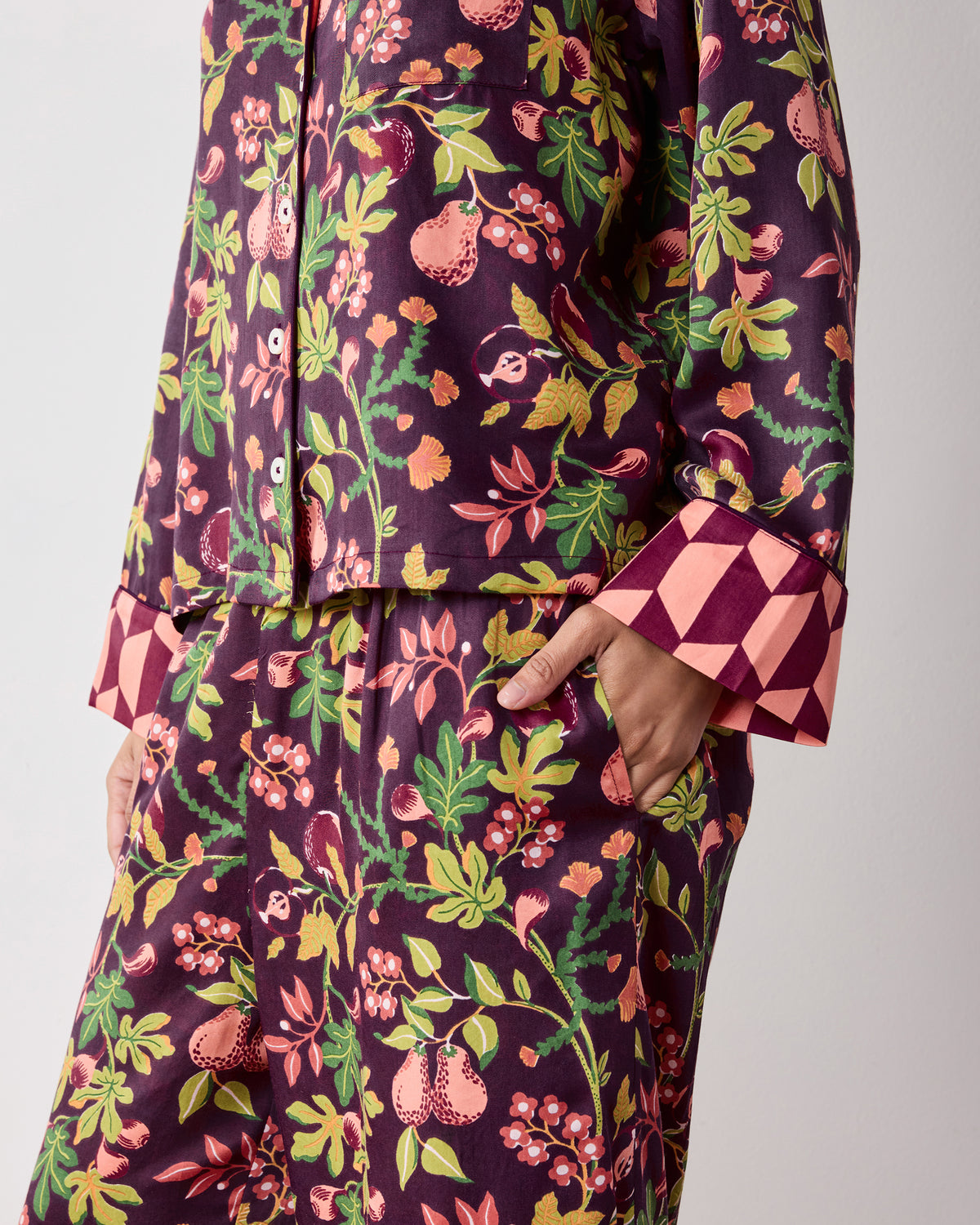 Close view of the plum Pomme & Poire Soho pajama set showing the button-front top, fruit-and-greenery print, side pocket, and contrasting cuff.