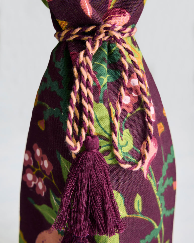 Close-up of the Pomme & Poire plum wine bag’s braided tie and tassel against its fruit-and-floral pattern.