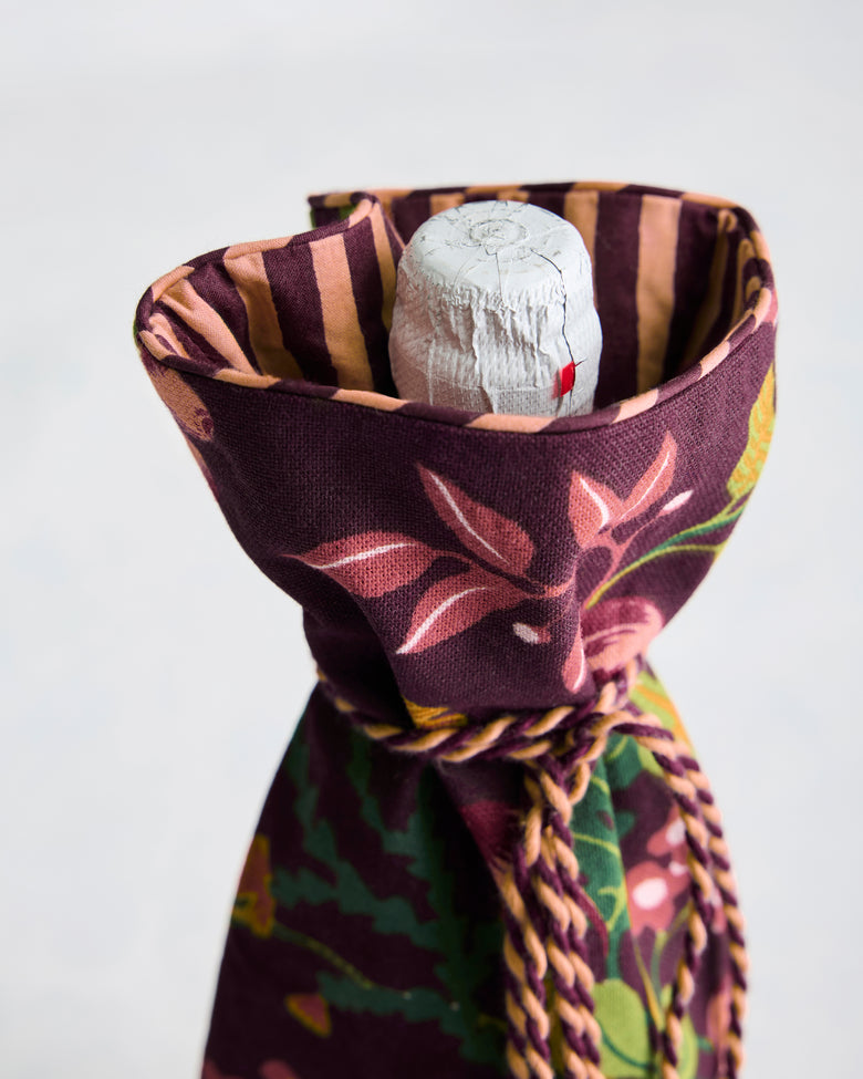 Pomme & Poire plum wine bag shown gathered around a bottle, with a striped lining visible at the opening and braided tassel tie.