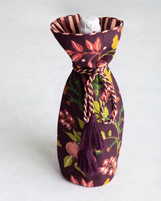 Plum floral wine bag holding a bottle, with a braided tie and tassels at the neck.