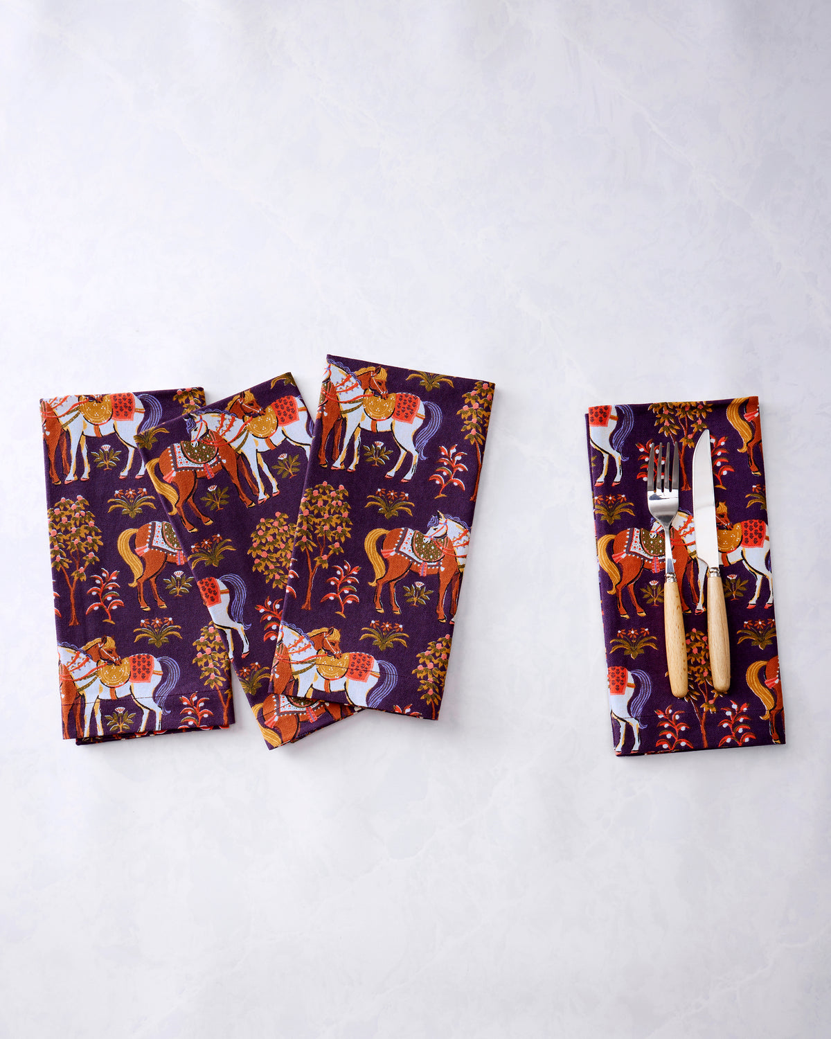 Four purple horse-print dinner napkins, with a fork and knife placed on one napkin.