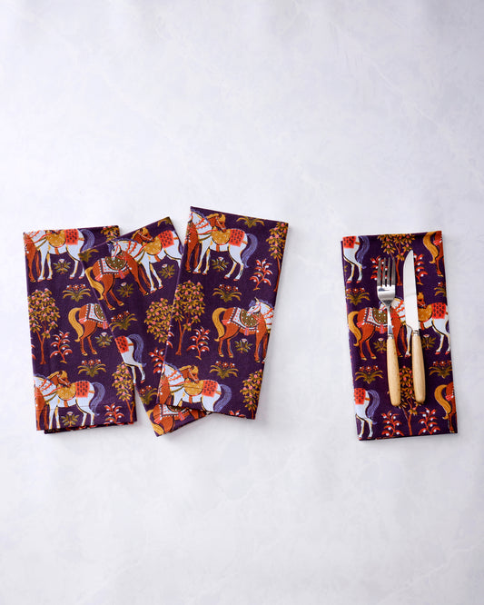 Four purple horse-print dinner napkins, with a fork and knife placed on one napkin.