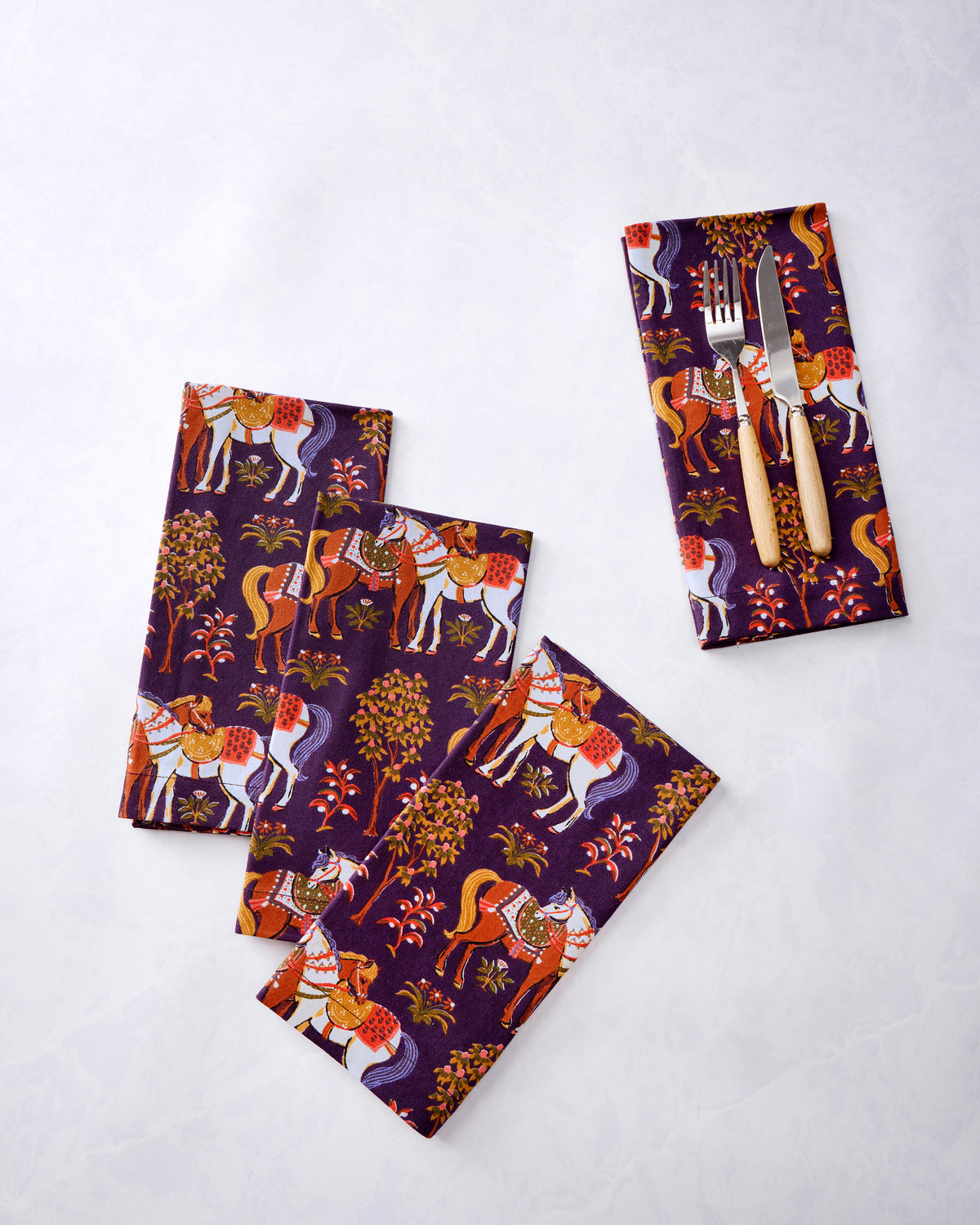 Four purple horse-print dinner napkins arranged separately, with a fork and knife on one napkin.