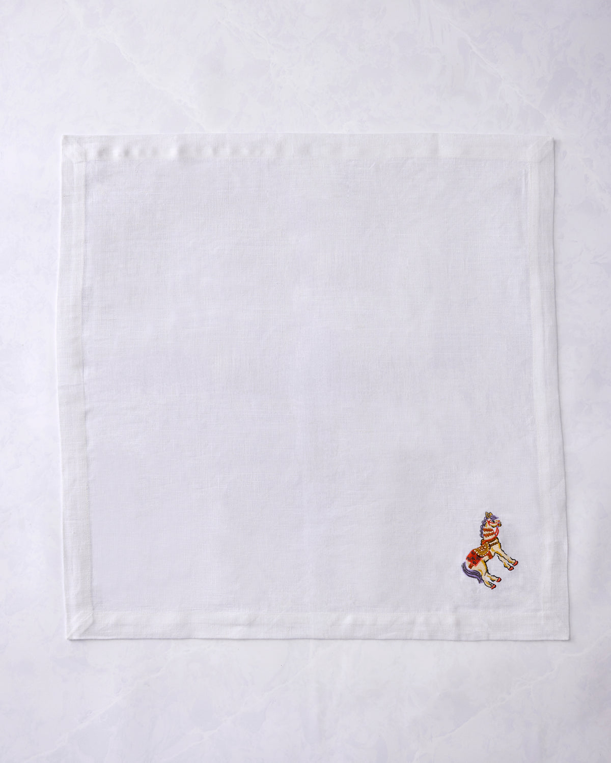 White square dinner napkin with a small embroidered horse near the lower-right corner.