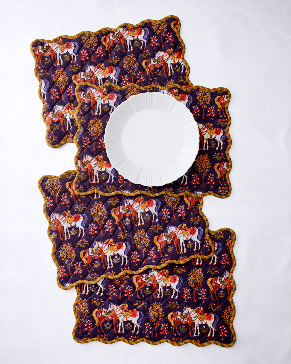 Four scalloped quilted horse-print placemats arranged with a white dinner plate on top.