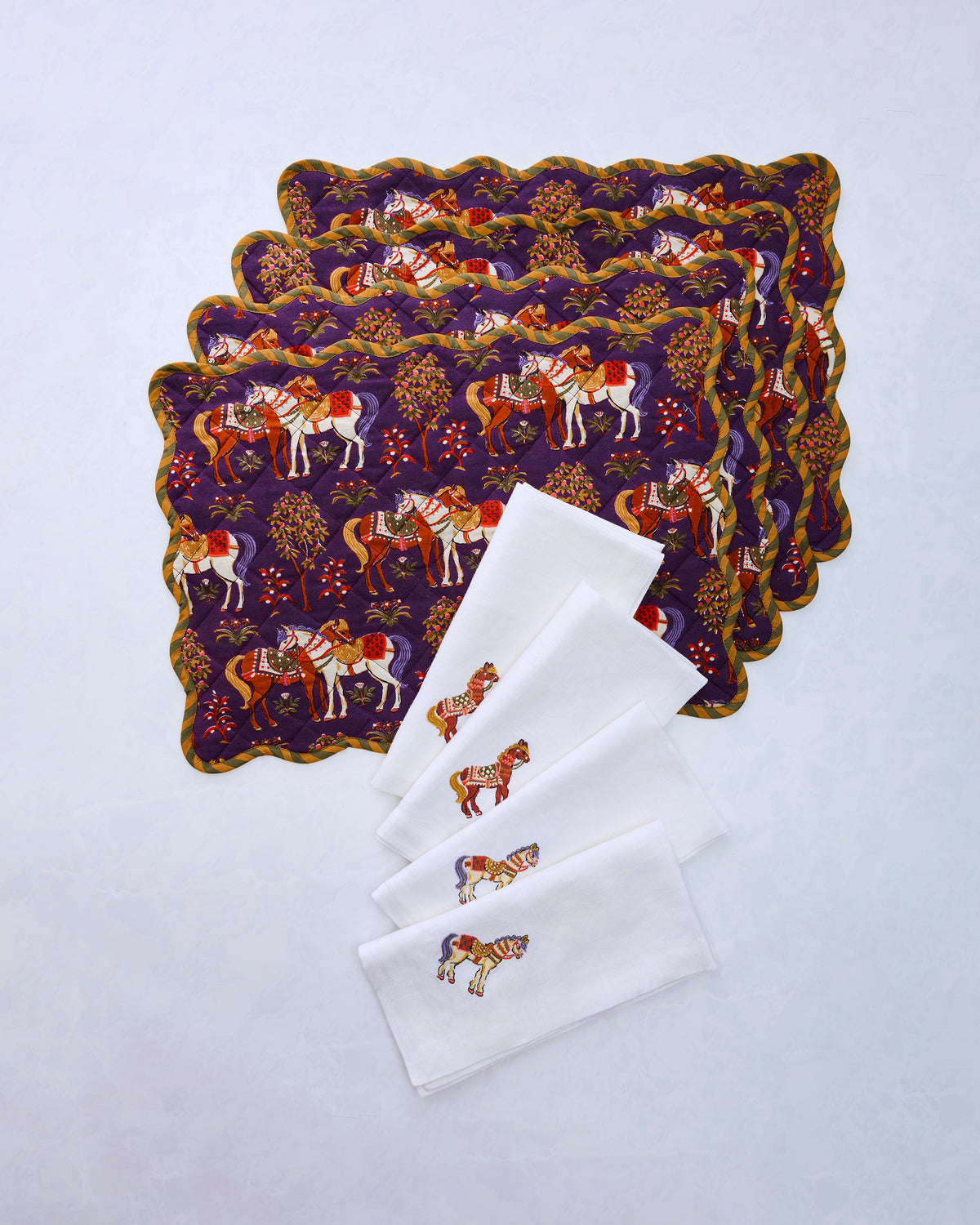 Bundle of four purple scalloped placemats with horse prints and four white napkins embroidered with horses.