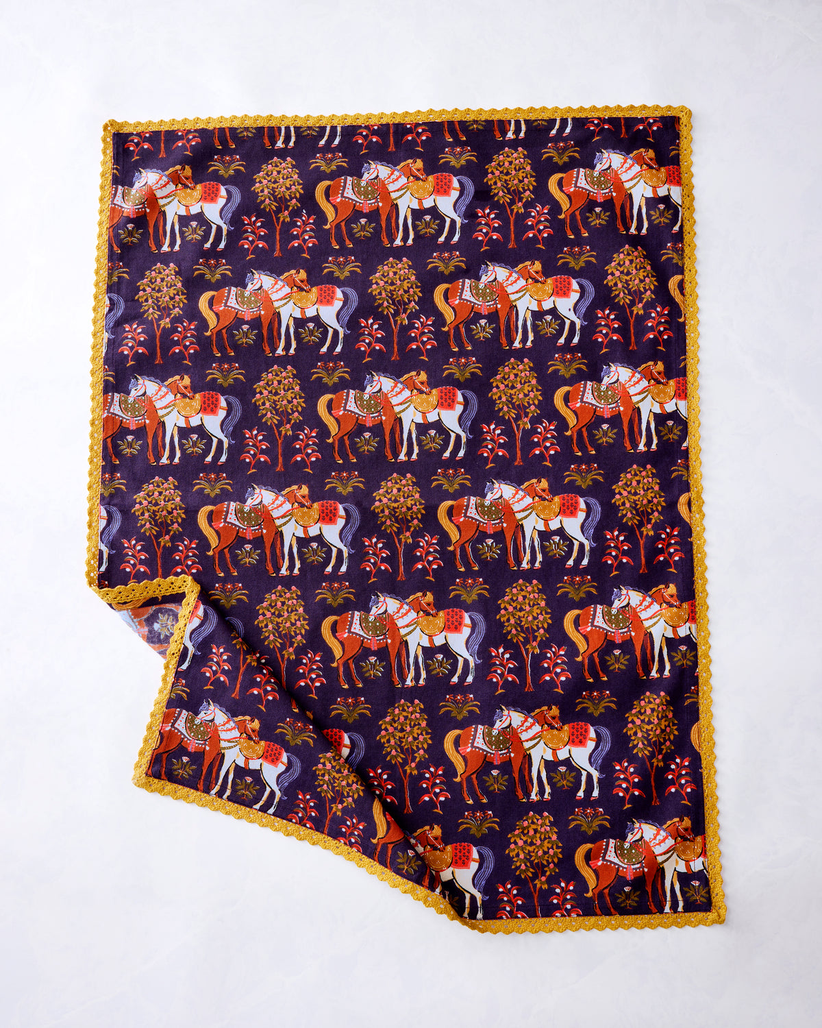 Deep aubergine kitchen towel with a repeating decorated-horse and tree print and scalloped gold trim, shown partially folded.