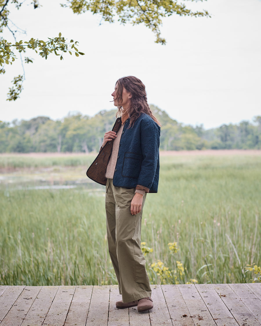 Full-length side view of the vintage indigo Elliott jacket worn with trousers beside a marsh.
