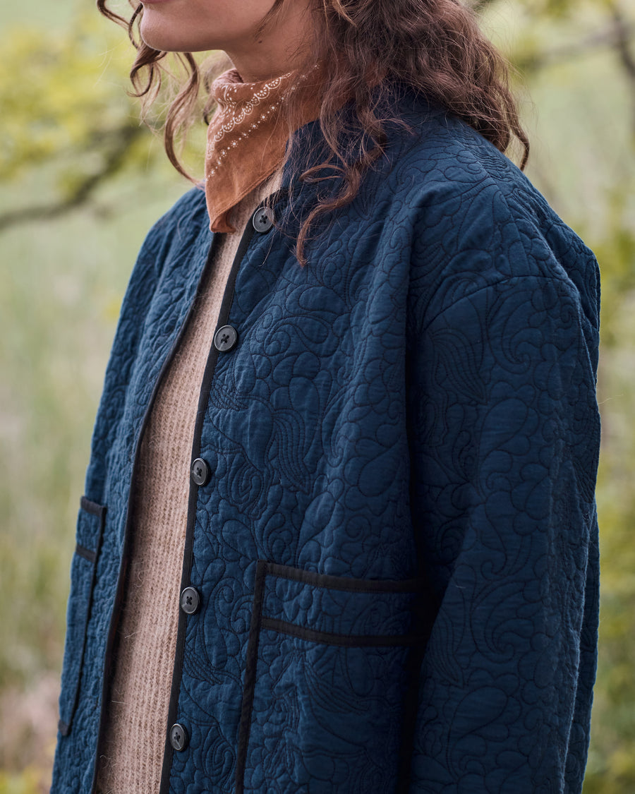 Close-up of the vintage indigo Elliott jacket showing its quilted equestrian pattern, front buttons, and trimmed patch pocket.