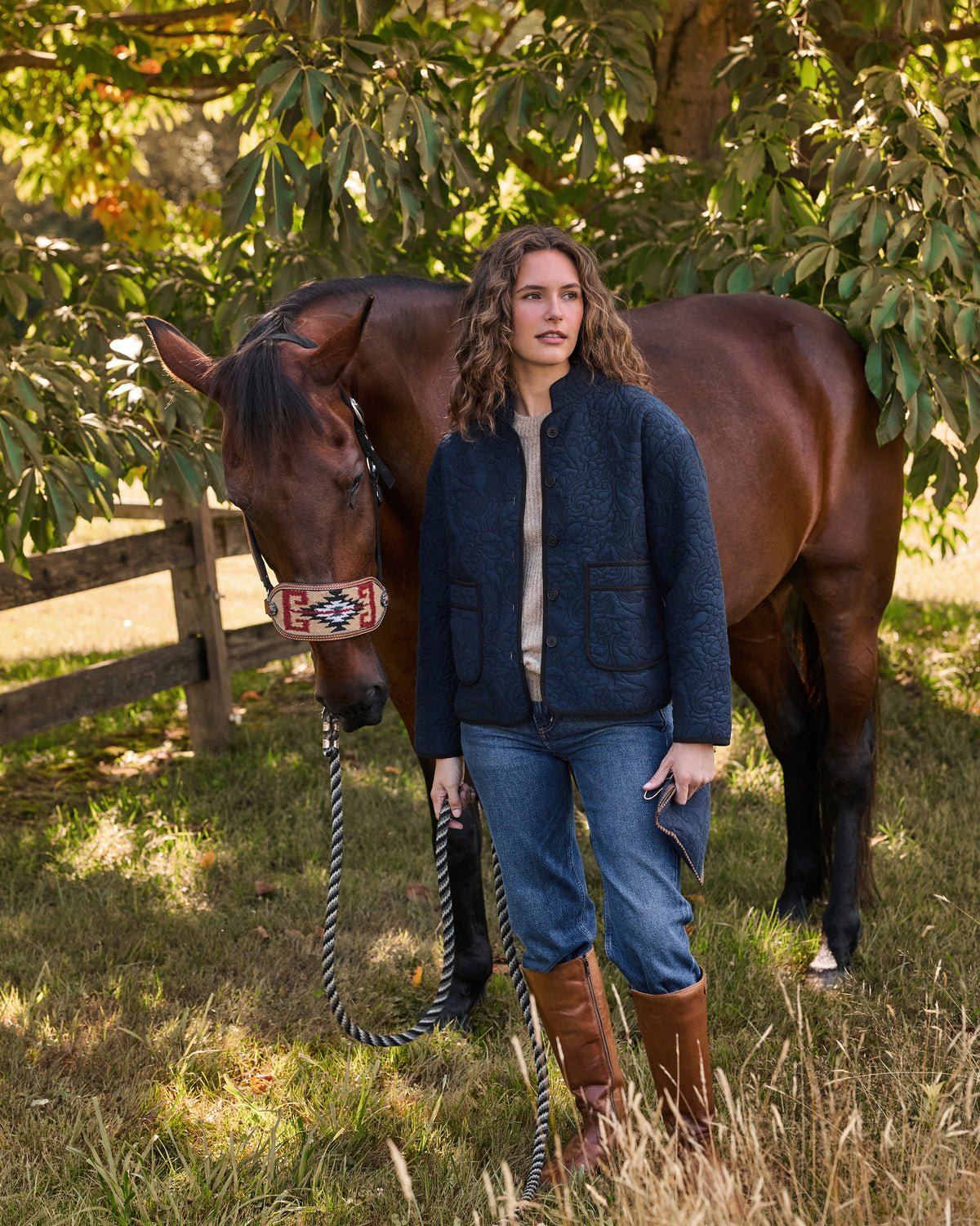 Person wearing a navy quilted jacket standing beside a brown horse outdoors.