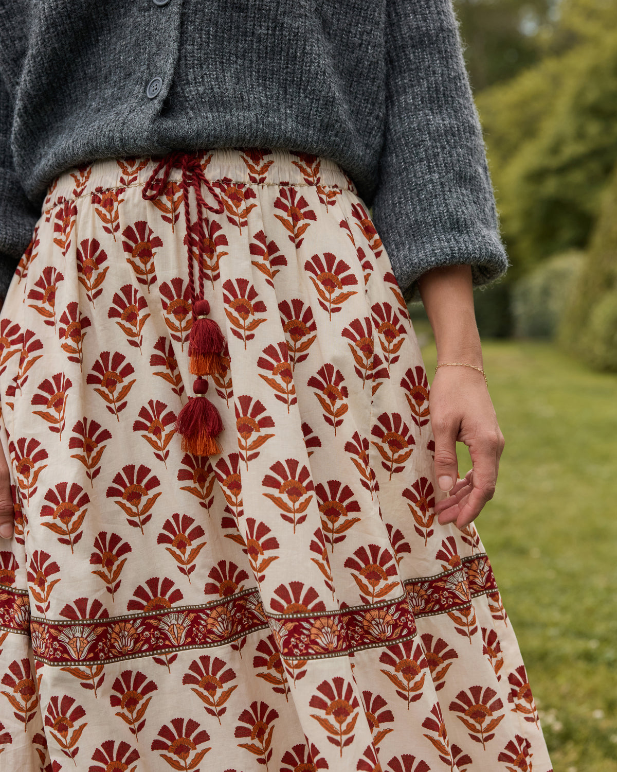 Close-up of the Sierra Bloom Carry On Skirt showing the red tassel tie, cream floral print, and decorative border band.
