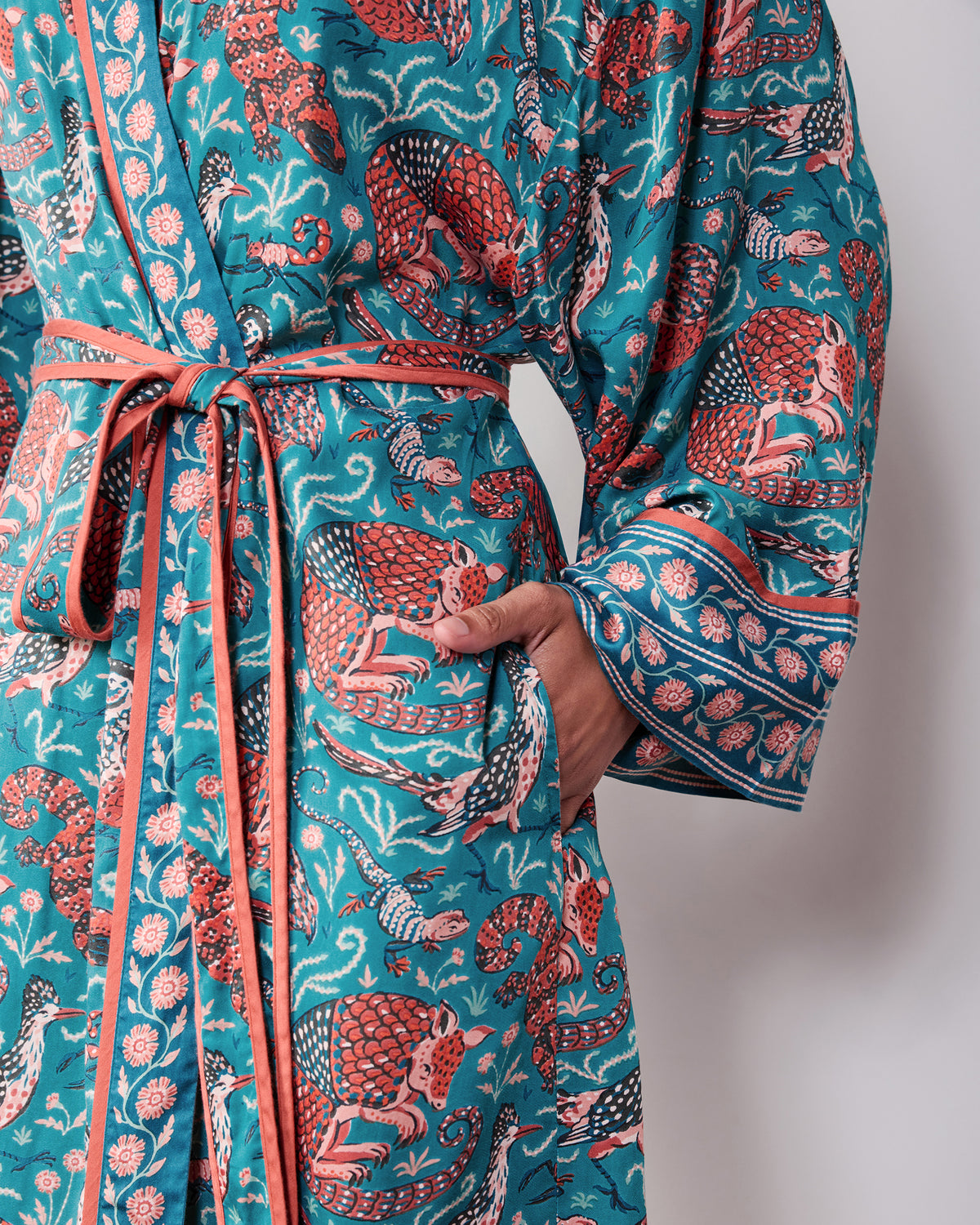Close-up of the teal Canyon Critters robe showing the tied belt, front pocket, patterned fabric, and contrast-trimmed sleeve cuff.