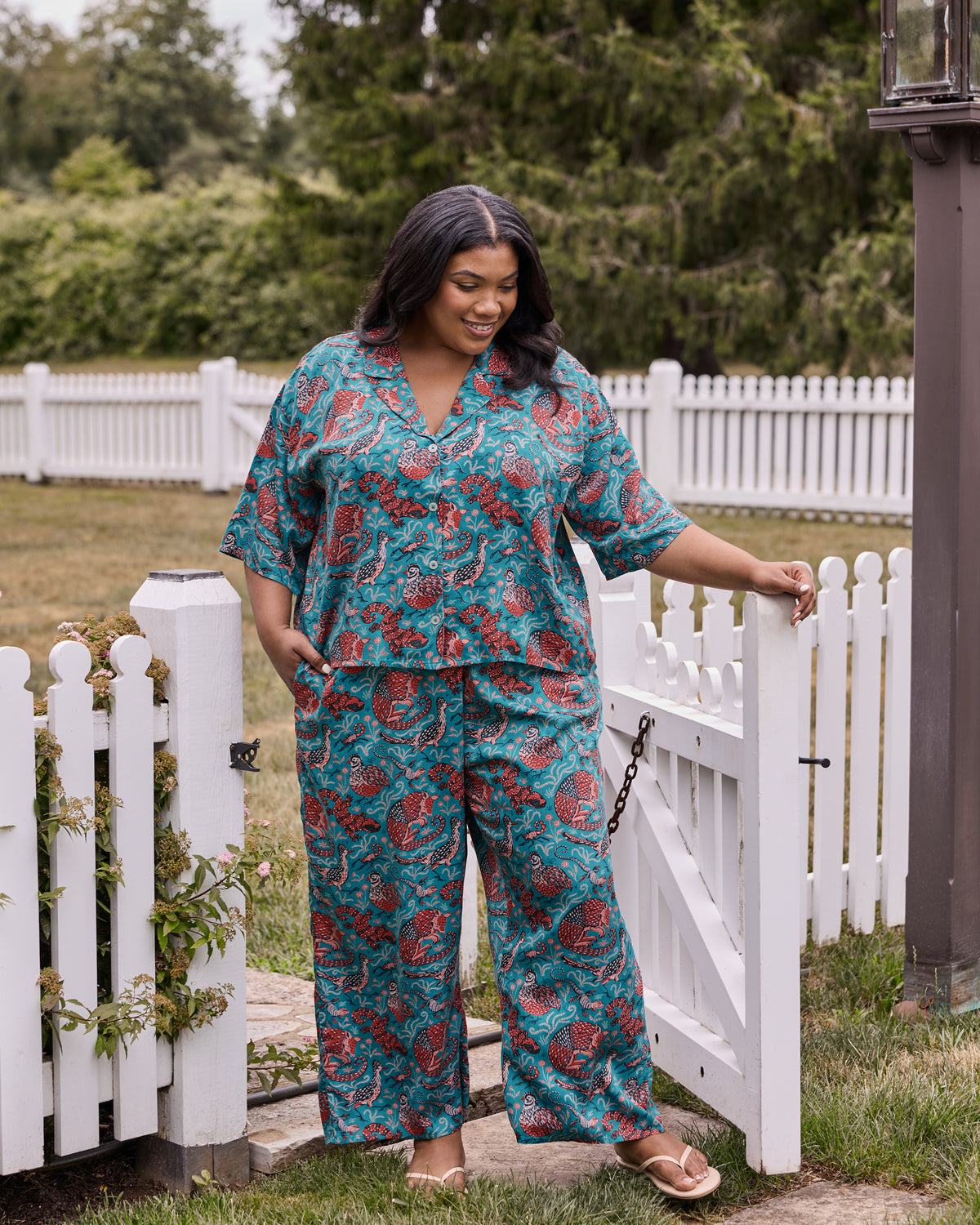 Full view of a teal printed pajama set with a short-sleeve top and wide-leg pants featuring lizards, birds, and armadillos.