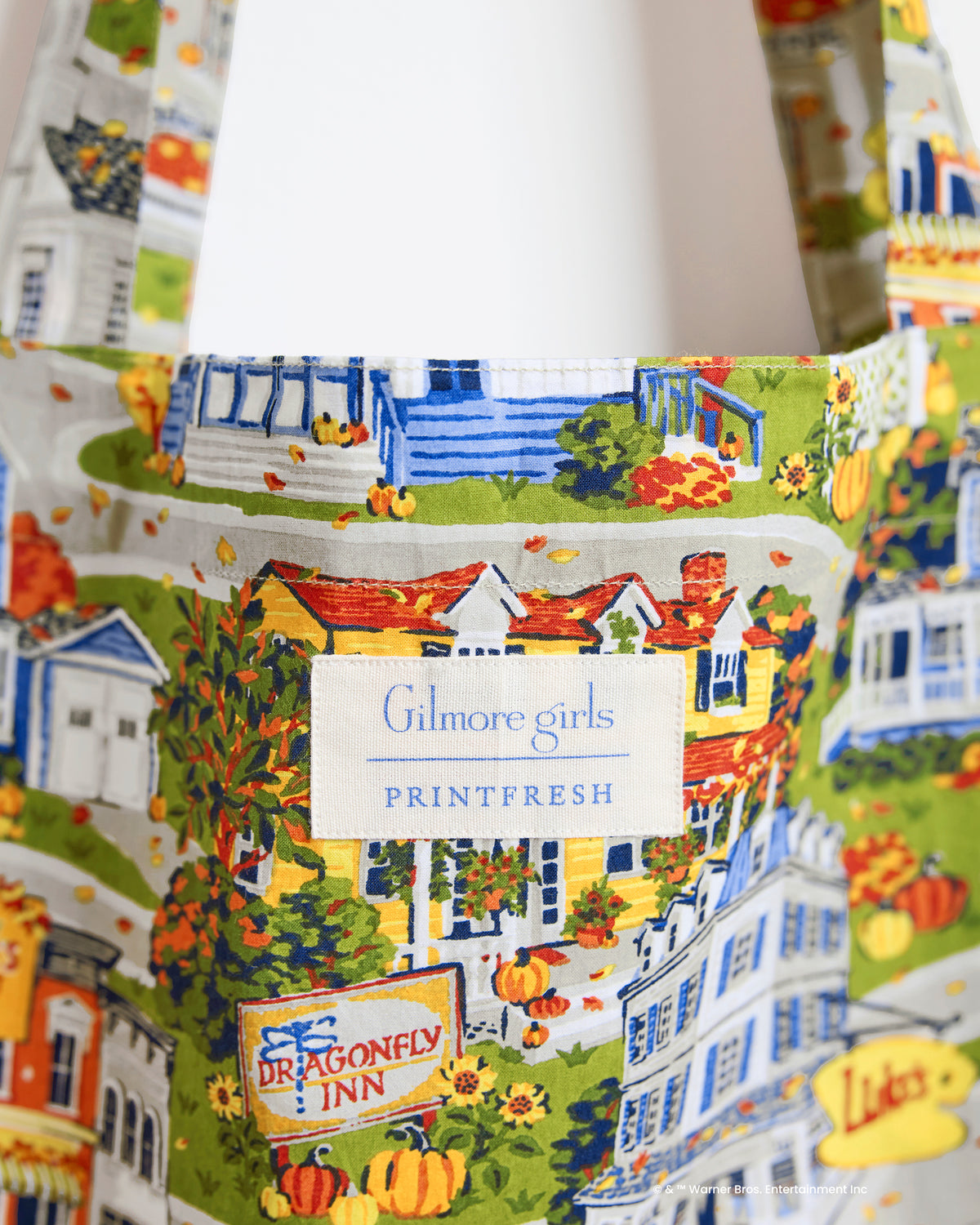 Close-up of the Stars Hollow harvest-festival tote showing the printed town scene, Dragonfly Inn sign, and Gilmore Girls Printfresh label.