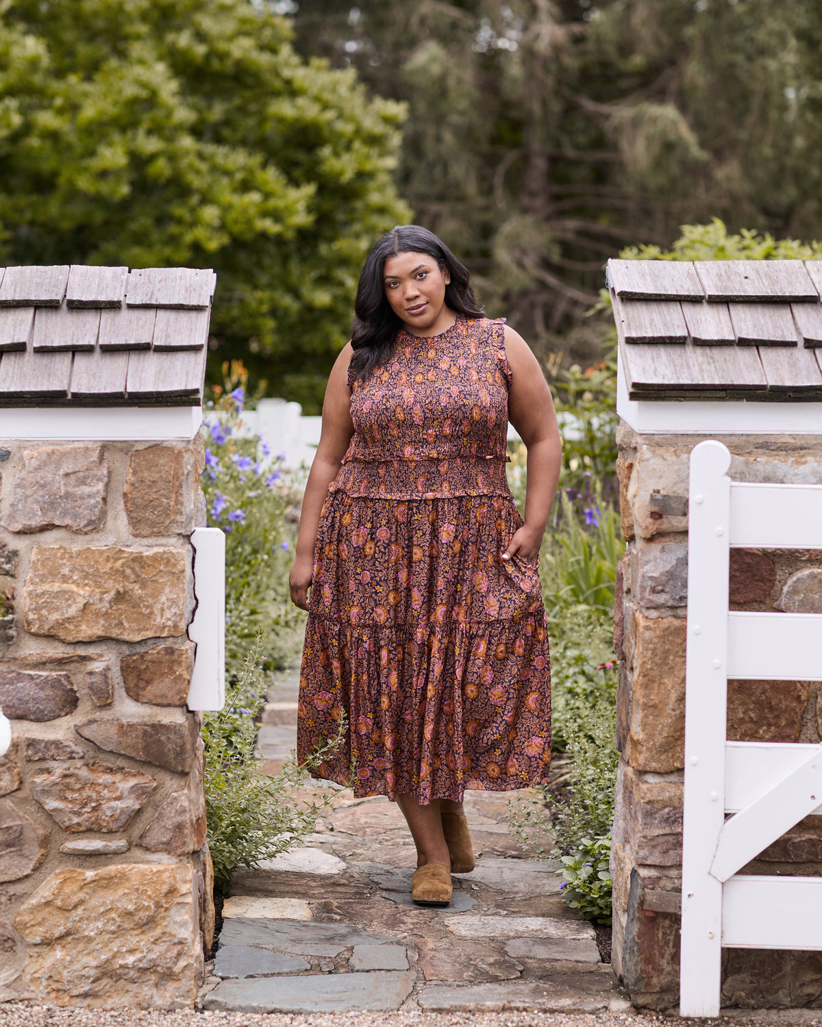 Full-length view of the Sunset Vine Ellis dress, showing the sleeveless bodice, smocked waist, tiered skirt, floral print, and side pockets.