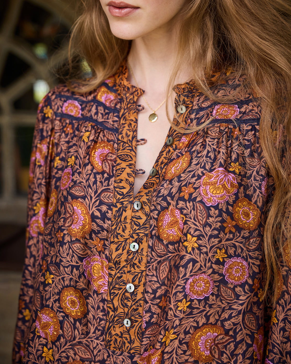 Close-up of the Evelyn blouse neckline and button placket, showing the floral print and pendant necklace.