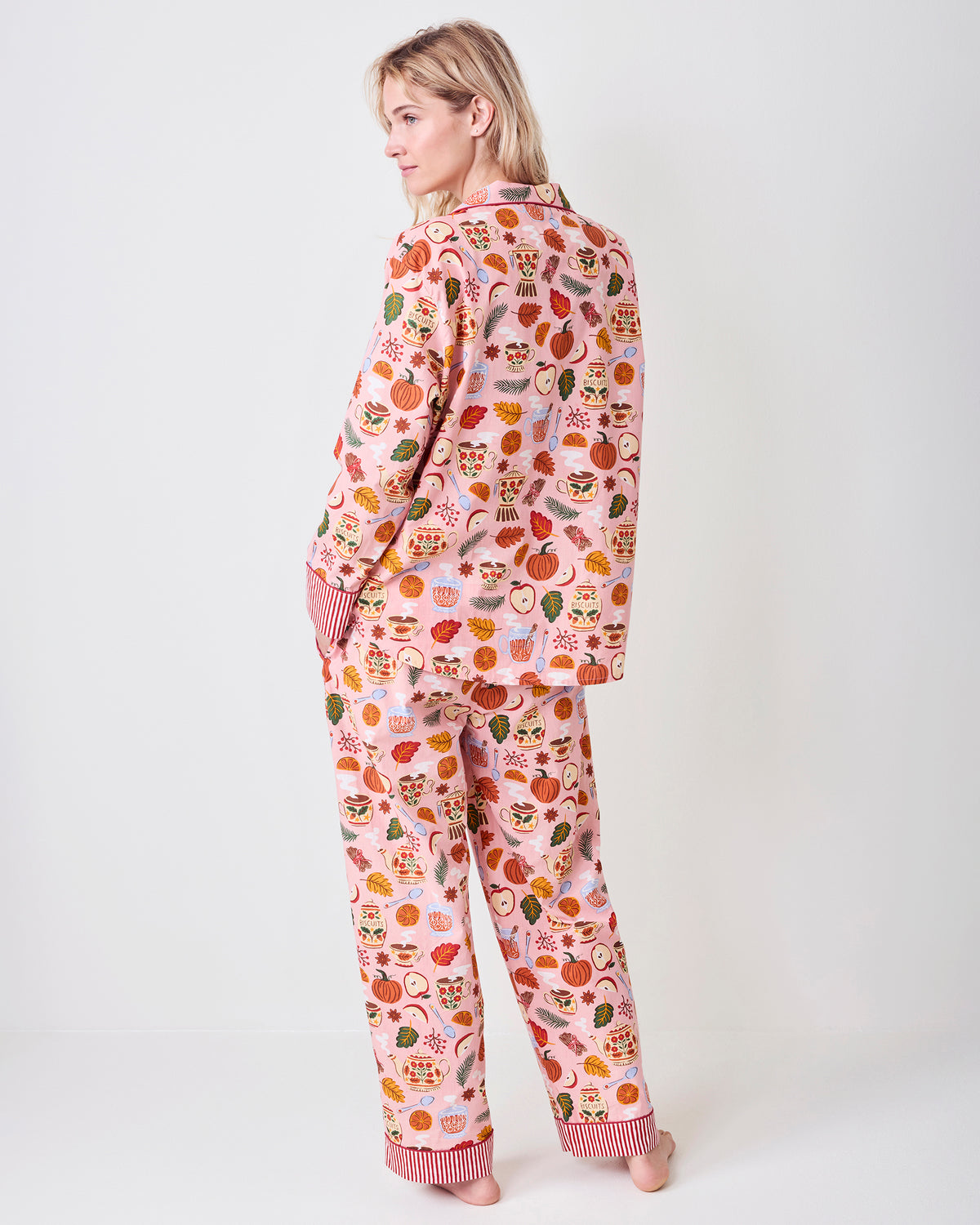 Back view of the pink Autumn Cafe long pajama set, showing the shirt hem, matching pants, striped cuffs, and allover tea, fruit, leaf, and biscuit-jar print.