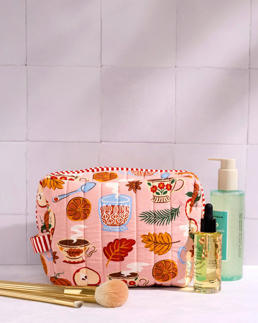 Pink quilted patterned pouch displayed with toiletries and makeup brushes on a tiled surface.