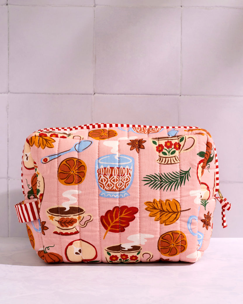 Front view of a pink quilted pouch with a printed tea-and-seasonal motif and contrasting striped trim.