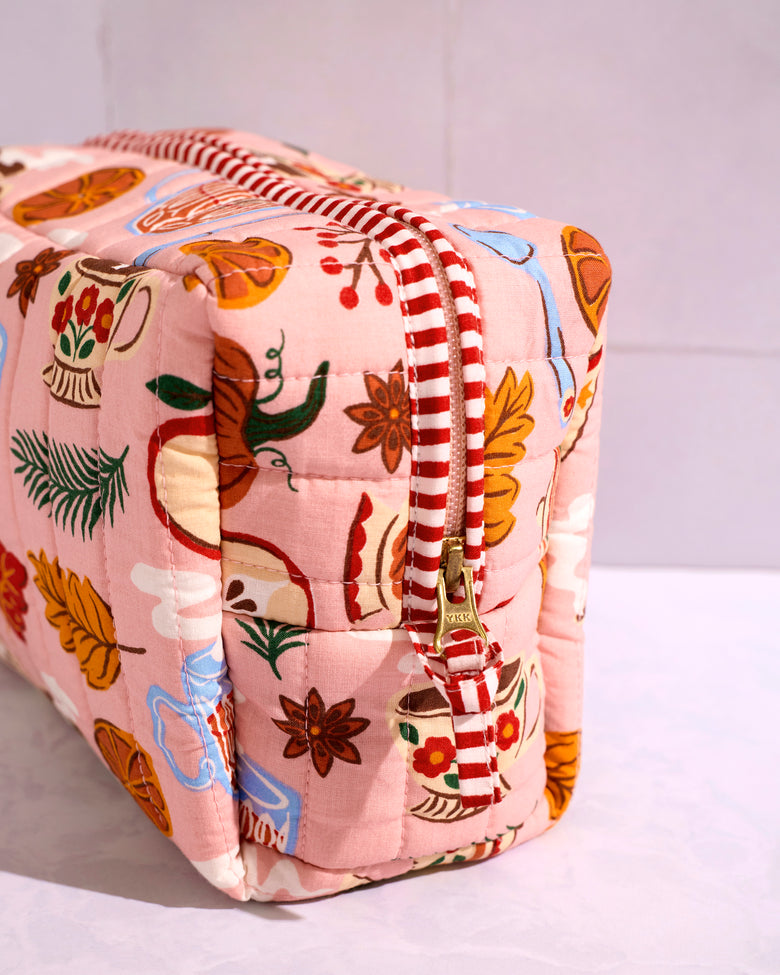 Close-up of the rose pink quilted pouch with a tea-themed print, red-and-white striped trim, and zipper closure.