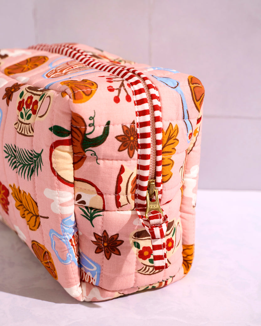Close-up of the rose pink quilted pouch with a tea-themed print, red-and-white striped trim, and zipper closure.