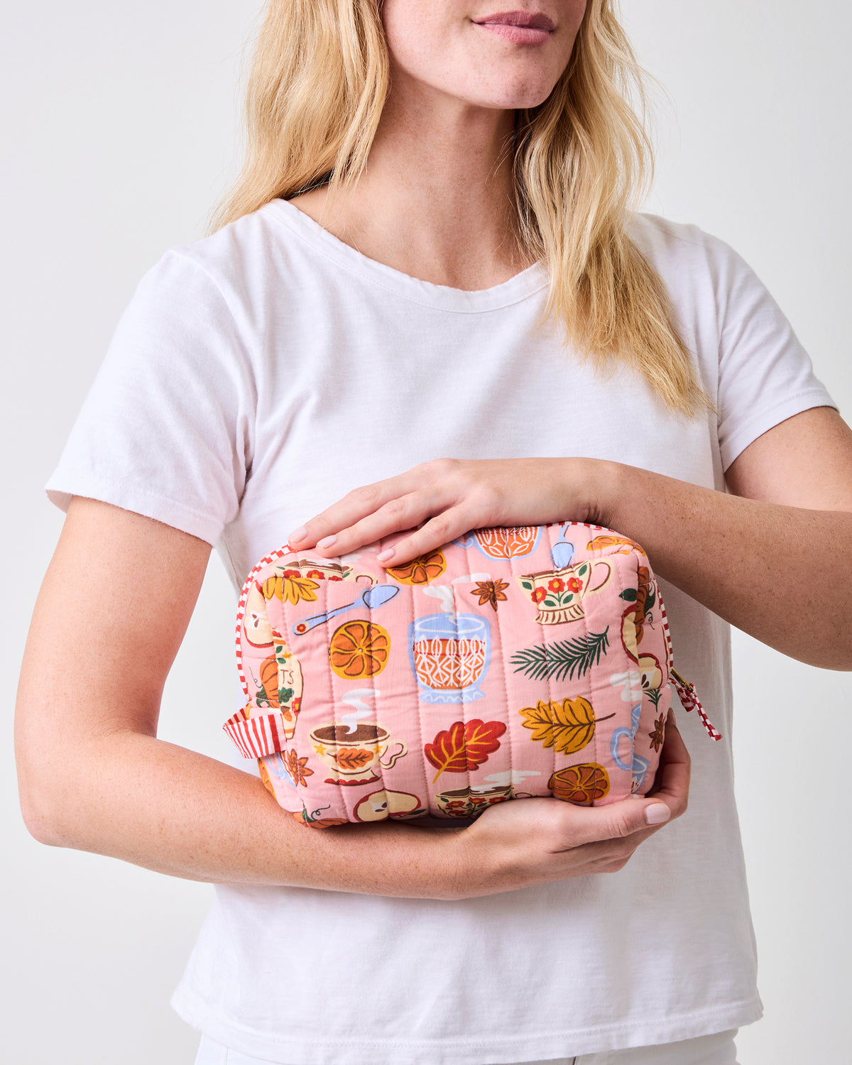Person holding the rose pink quilted tea-print pouch horizontally.