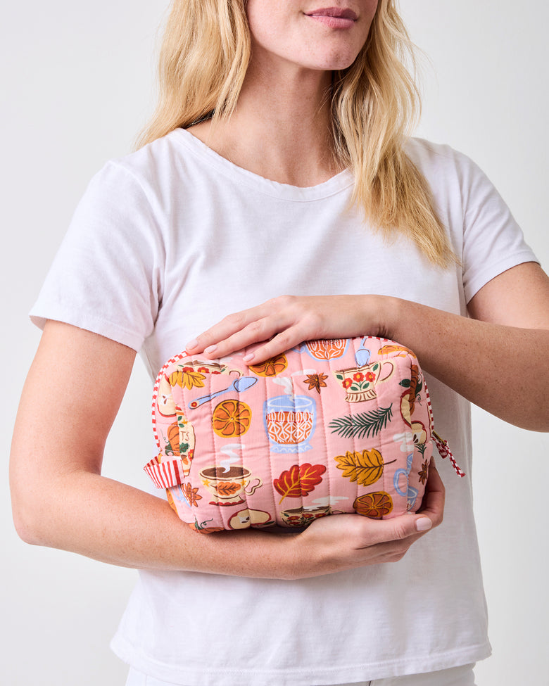 Person holding the rose pink quilted tea-print pouch horizontally.