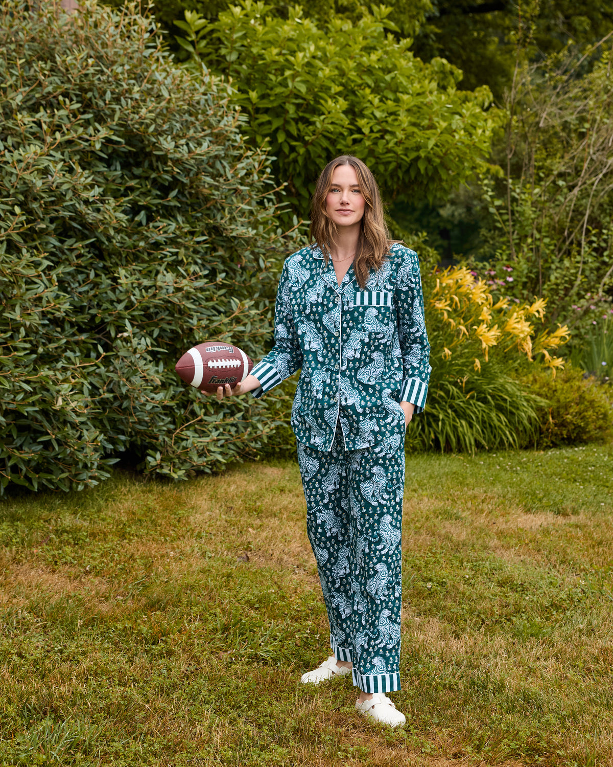 Full-length view of a Game Day Green Tiger Queen long pajama set worn outdoors, with a button-down top, drawstring pants, striped cuffs, and a football.