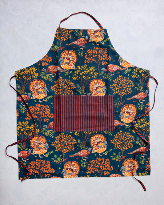 Navy Turkey Trot apron with turkey-and-tree pattern, striped neck strap, waist ties, and front pocket.
