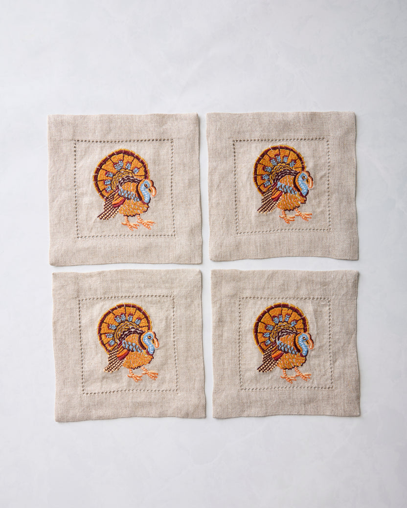 Set of four natural cocktail napkins, each embroidered with a colorful turkey motif.