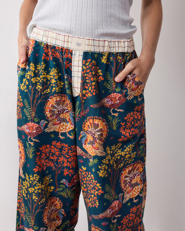 Close-up front detail of the navy Turkey Trot pajama pants showing the plaid waistband, button fly, pockets, and turkey print.